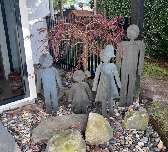 Four steel family silhouettes installed around a Japanese maple in a landscaped garden