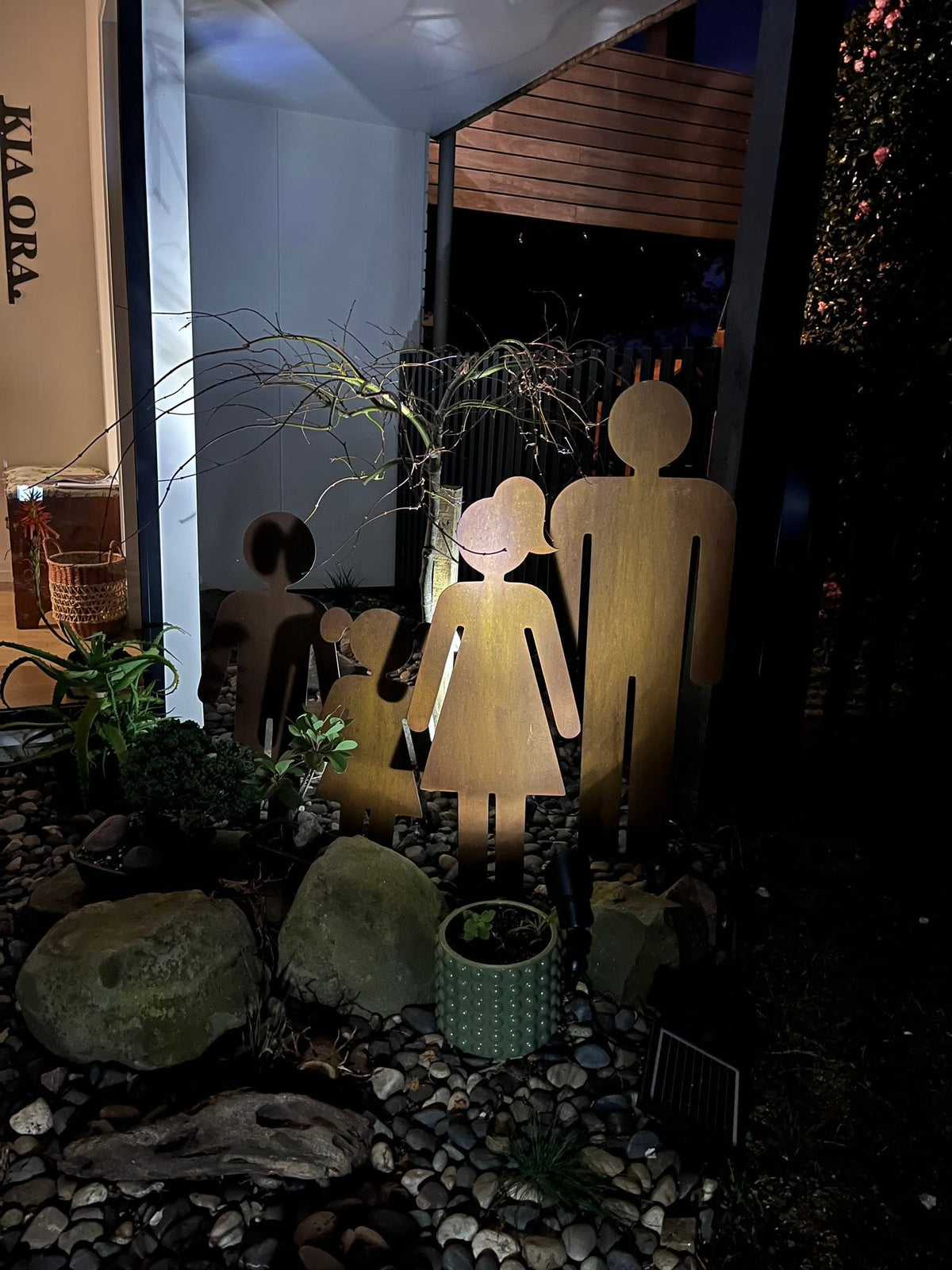 Corten steel family silhouette garden sculptures illuminated in an evening garden