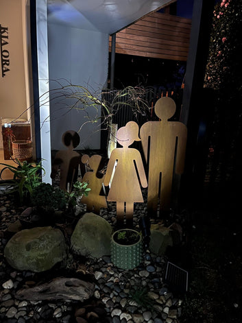 Corten steel family silhouette garden sculptures illuminated in an evening garden